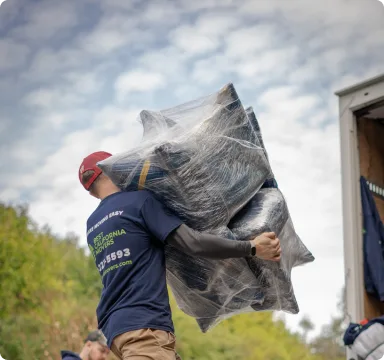 Mover carrying shrink-wrapped furniture out of a house
